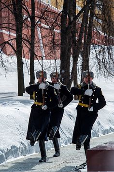 three men in uniform marching down the street with trees and snow on the ground behind them