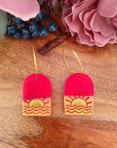 pink and yellow earrings with sun design on them sitting on a wooden table next to flowers