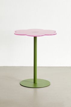 a pink and green table sitting on top of a cement floor next to a white wall