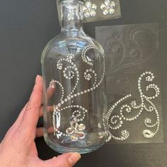 a hand is holding a glass bottle with diamond embellishments