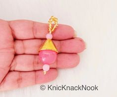 a hand holding a tiny pink beaded necklace with a gold cone on it's end