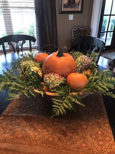 a bowl filled with oranges and greenery on top of a wooden dining room table