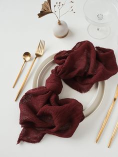 a white plate topped with a red scarf next to utensils and goldware