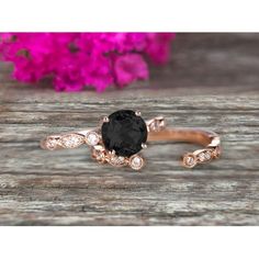 an oval black diamond ring set on top of a wooden table with pink flowers in the background