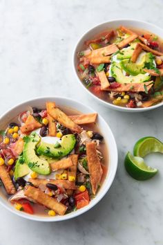 two white bowls filled with mexican soup next to an avocado slice on the side