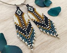 the beaded earrings are hanging from a string on a wooden table next to green leaves