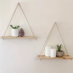 two wooden shelves with candles and plants on them hanging from the wall in front of a white wall