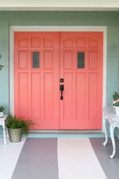 the front door is painted coral pink and has two planters with flowers in them