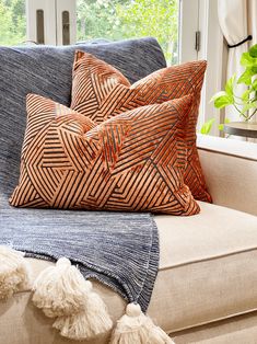 two decorative pillows on a couch in front of a window