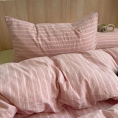 an unmade bed with pink and white striped sheets, pillows and a black cat