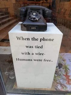 an old fashioned phone sitting on top of a sign in a store window that says, when the phone was tied with a wire humans were free