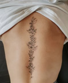 a woman's lower back tattoo with flowers on her left side ribcage