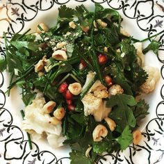 a white plate topped with greens and cauliflower on top of a black and white table cloth