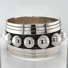 "The last time we had anything similar to this fabulous bracelet in the Studio it wasn't there very long! It is a statement bracelet if there ever was one! The bangle was handmade by a very talented artisan in Taxco, Mexico. The sterling silver hinged bangle features raised dots that graduate in size as it twists on the wrist. The oxidized center really makes the dots pop. Get ready for the compliments when people say \"I love your bracelet!\"" Unique Bangle With Polished Finish, Unique Round Bangle With Polished Finish, Unique Round Cuff Bracelet With Polished Finish, Unique Sterling Silver Oyster Bangle Bracelet, Modernist Handmade Cuff Bangle Bracelet, Adjustable Modernist Bangle Bracelet, Unique Stackable Cuff Bangle Bracelet, Handmade Modernist Bangle Jewelry, Adjustable Round Modernist Bracelets