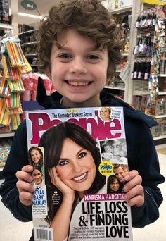 a young boy holding up a magazine in front of his face and smiling at the camera