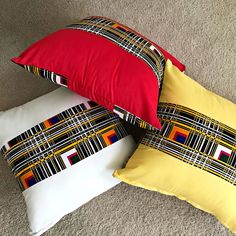 three pillows are sitting on the floor next to each other, one is yellow and the other is red