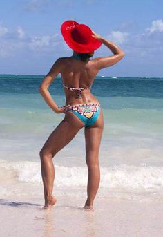 a woman in a red hat is standing on the beach and looking at the water