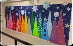 an art project with colorful paper trees and snowflakes hanging from the side of a wall