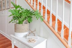 a white table with a plant on it next to a banister and some pictures