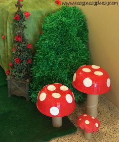 two red mushrooms sitting on the ground next to a green bush and potted plant