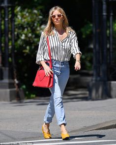 a woman walking across the street with a red purse in her hand and yellow shoes