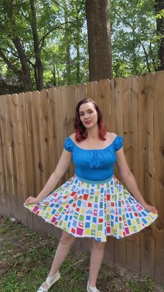 a woman standing in front of a wooden fence wearing a dress with colorful squares on it