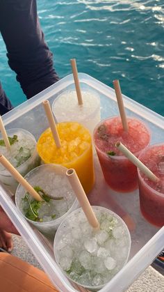 there are many drinks on the tray by the water and someone is holding it in their hand