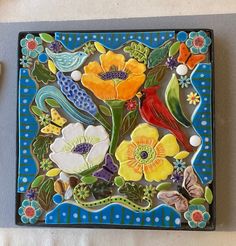 a colorful tile with flowers and birds on it, next to a pair of scissors