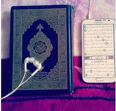 an electronic device is next to a book on a purple blanket, with ear buds in the foreground