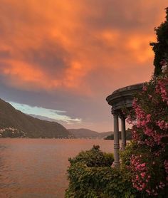 a beautiful sunset over the water with pink flowers and trees in bloom on either side