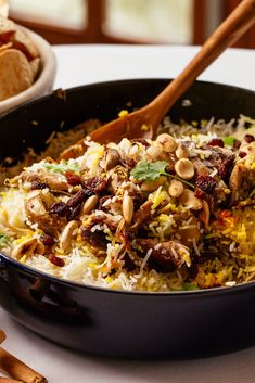 a pan filled with rice and meat on top of a table next to some bread