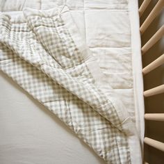 an unmade crib bed with white sheets and checkered comforter on it