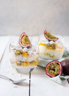 two desserts with fruit and whipped cream in them on a white wooden table next to a spoon