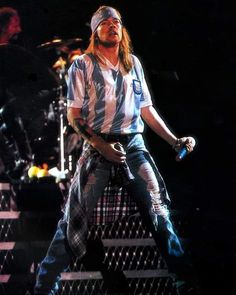 a man standing on top of a stage holding a microphone in his right hand and wearing a bandana