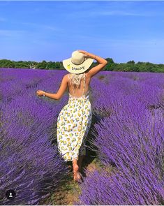 a woman walking through a lavender field with her back to the camera, wearing a sun hat