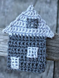 a crocheted house is hanging on a wooden post