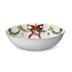 a white bowl with a bow and holly decorations on it, sitting on a white surface