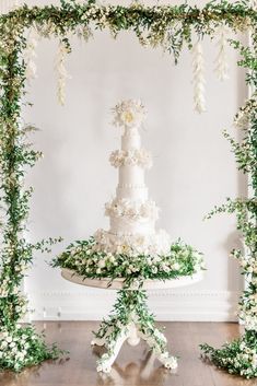 a white wedding cake sitting on top of a table covered in flowers and greenery