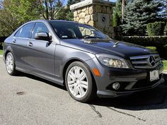 a mercedes c - class is parked in front of a stone pillar with a clock on it