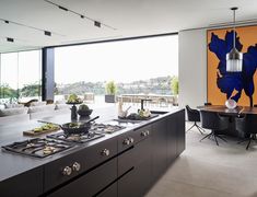 a kitchen with an island, stove top and dining table in front of large windows