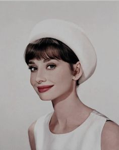 a woman wearing a white hat and smiling at the camera with her hair in a bun