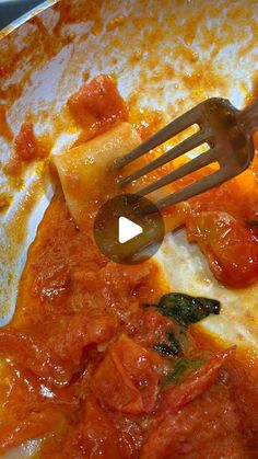 a fork is being used to stir up food in a pan with tomato sauce and spinach