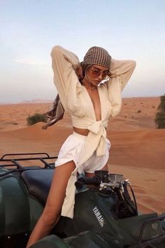 a woman sitting on top of a vehicle in the desert