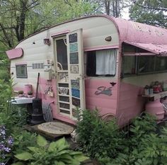 an old pink and white trailer is parked in the woods next to some purple flowers