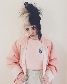 a woman with black hair wearing a pink shirt and white skirt is standing in front of a wall