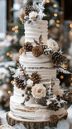 a white wedding cake with pine cones and flowers on top is surrounded by christmas trees