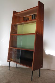 a wooden book shelf with glass doors on it's sides and black metal legs