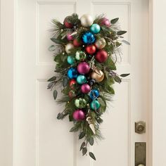 a christmas wreath on the front door with ornaments hanging from it's side,