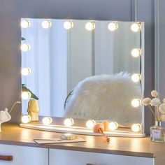 a vanity mirror with lights on it in front of a white dresser and flower vase