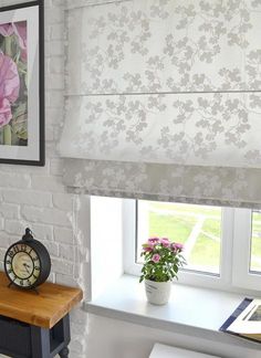 a white brick wall with pink flowers on the window sill next to a clock